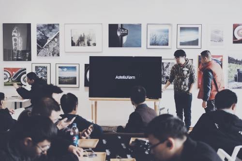 Man giving a presentation to several other people in front of a television.